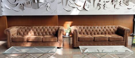 Un salón moderno con un sofá de cuero marrón, dos mesas de centro de cristal y una pared decorativa con formas recortadas.