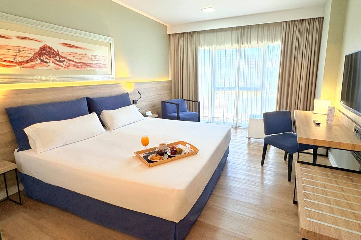 Ein Hotelzimmer mit einem großen Bett, einem Schreibtisch, einem Stuhl und einem Fernseher.
