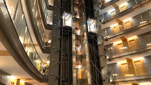 Een meerlaags atrium met glazen balustrades, liften en een centrale kolom met decoratieve details.