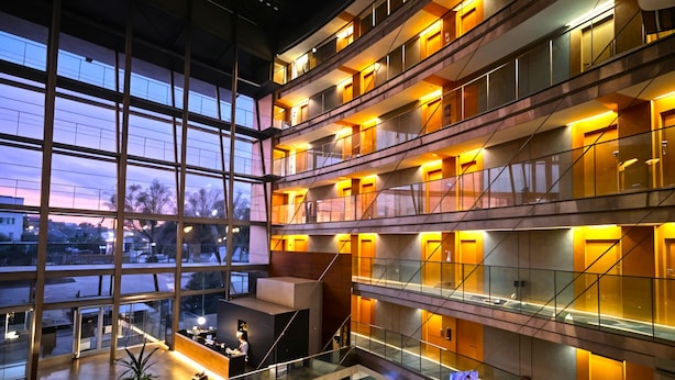 Hotelinterieur met meerdere verdiepingen, glazen balustrades, een centraal atrium en uitzicht op de omgeving bij zonsondergang.