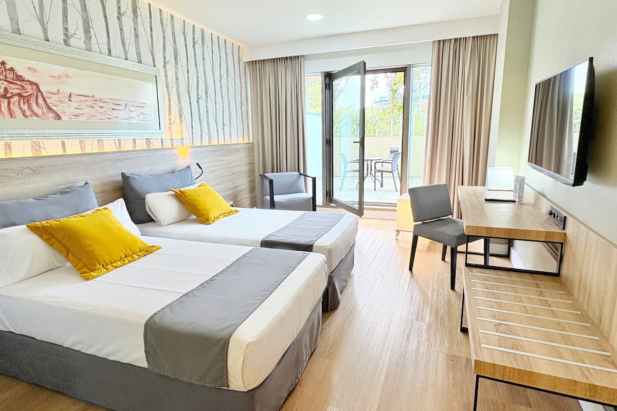 Een hotelkamer met twee bedden, een bureau, een stoel, een televisie en een balkon met gordijnen.