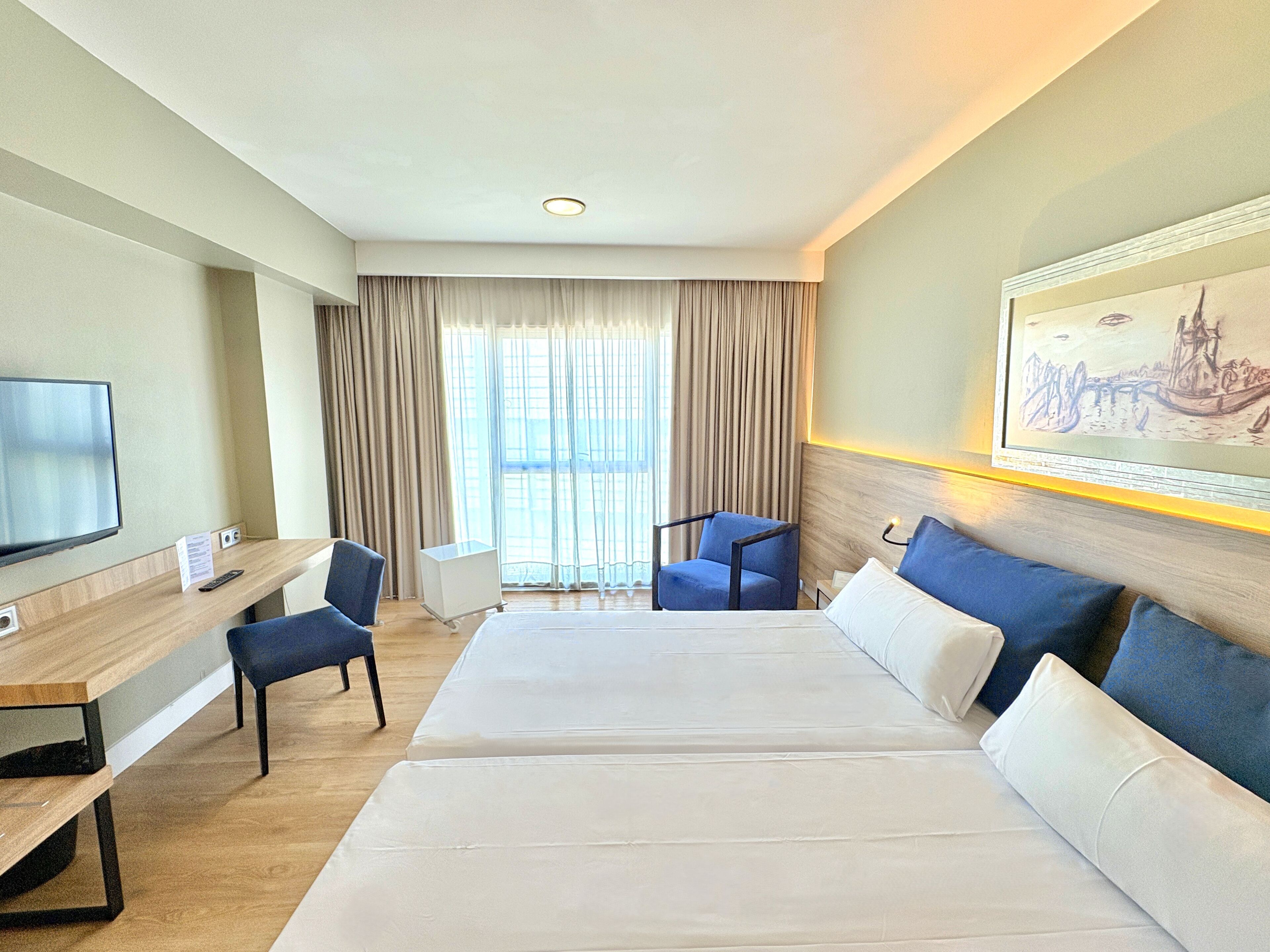 A hotel room with a large bed, a desk with a chair, a television, and a painting on the wall.