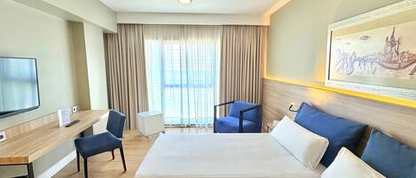 A hotel room with a large bed, a desk with a chair, a television, and a painting on the wall.
