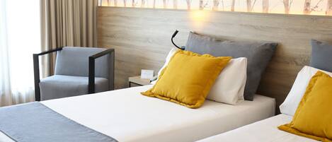 Una habitación de hotel con dos camas, una mesita de noche, una silla y un cuadro en la pared.
