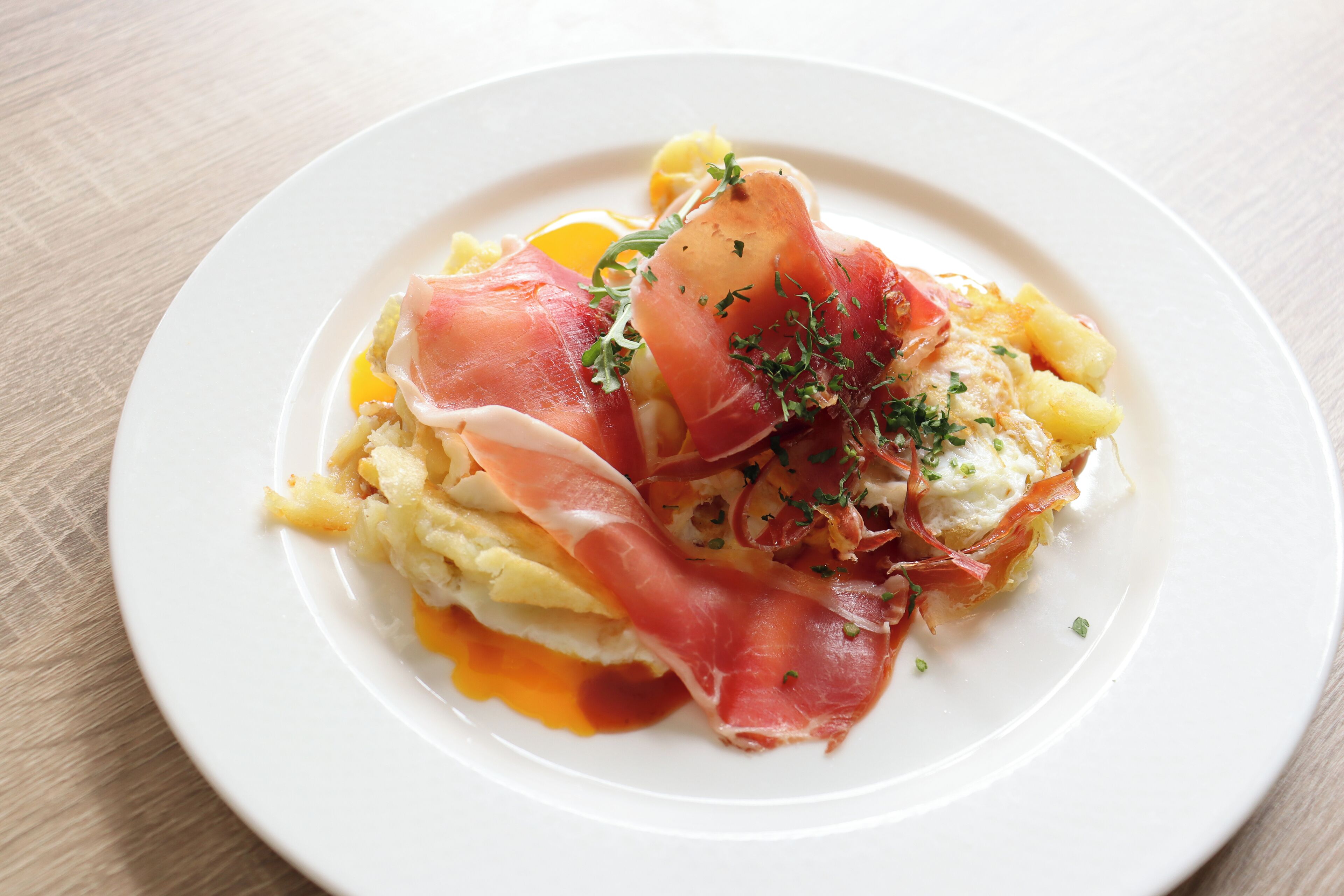 A plate of food with eggs, prosciutto, and herbs.