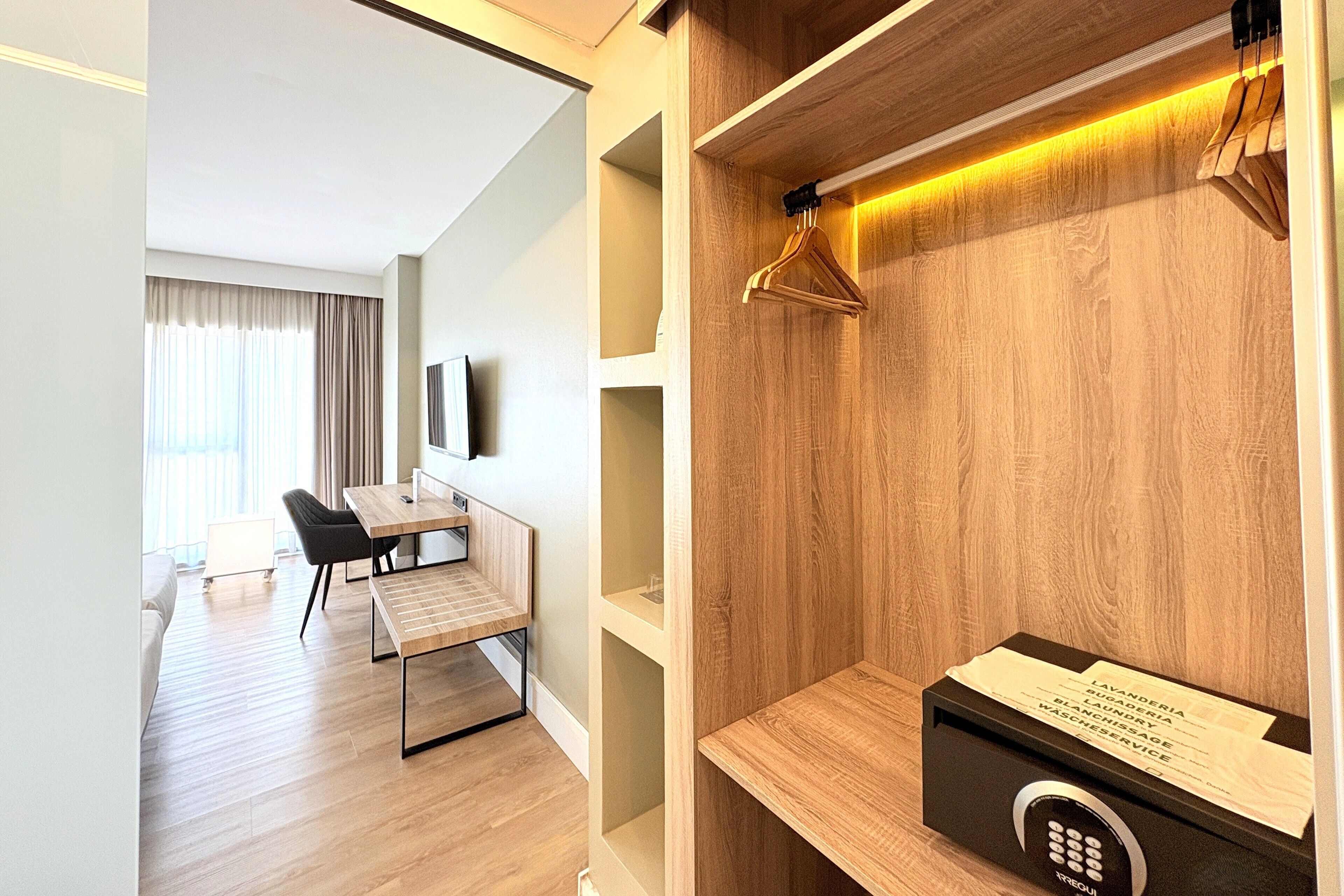 A modern hotel room with a wooden wall, a desk, a chair, and a hanging wooden hanger.