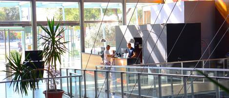 A modern interior with glass railings, a reception desk, and potted plants.