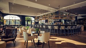 A modern bar area with a curved counter, multiple seating options including bar stools and chairs, and a large window offering a view of the outdoors. - Van Der Valk Hotel Melle - Osnabrück (Melle)