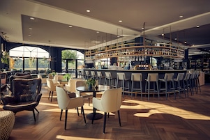 Un espace bar moderne doté d’un comptoir incurvé, de plusieurs options d’assises, notamment des tabourets et des chaises de bar, et d’une grande fenêtre offrant une vue sur l’extérieur.