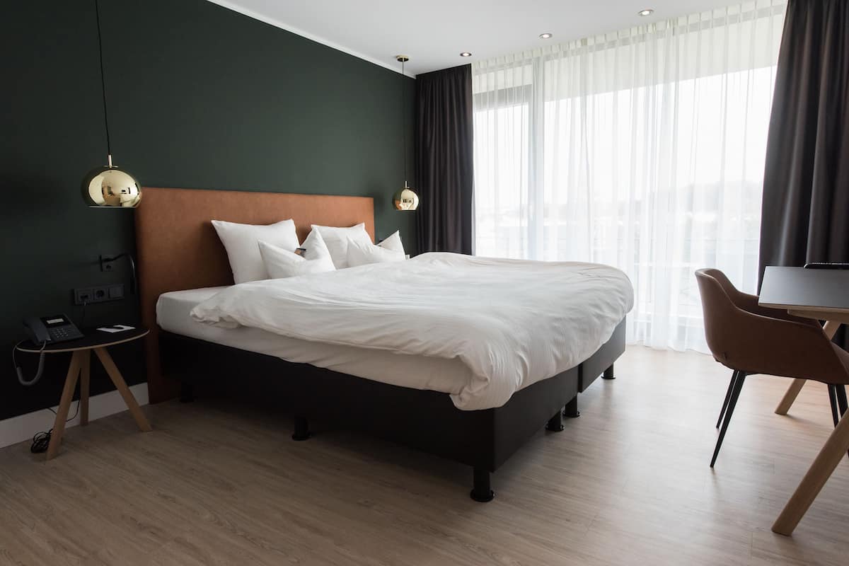 A modern hotel room with a large bed, a desk, and a chair.