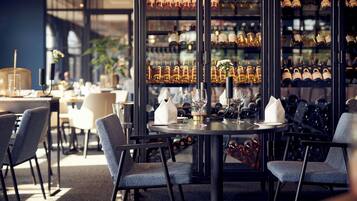 A restaurant interior with a round table, chairs, wine glasses, and a wine rack in the background.