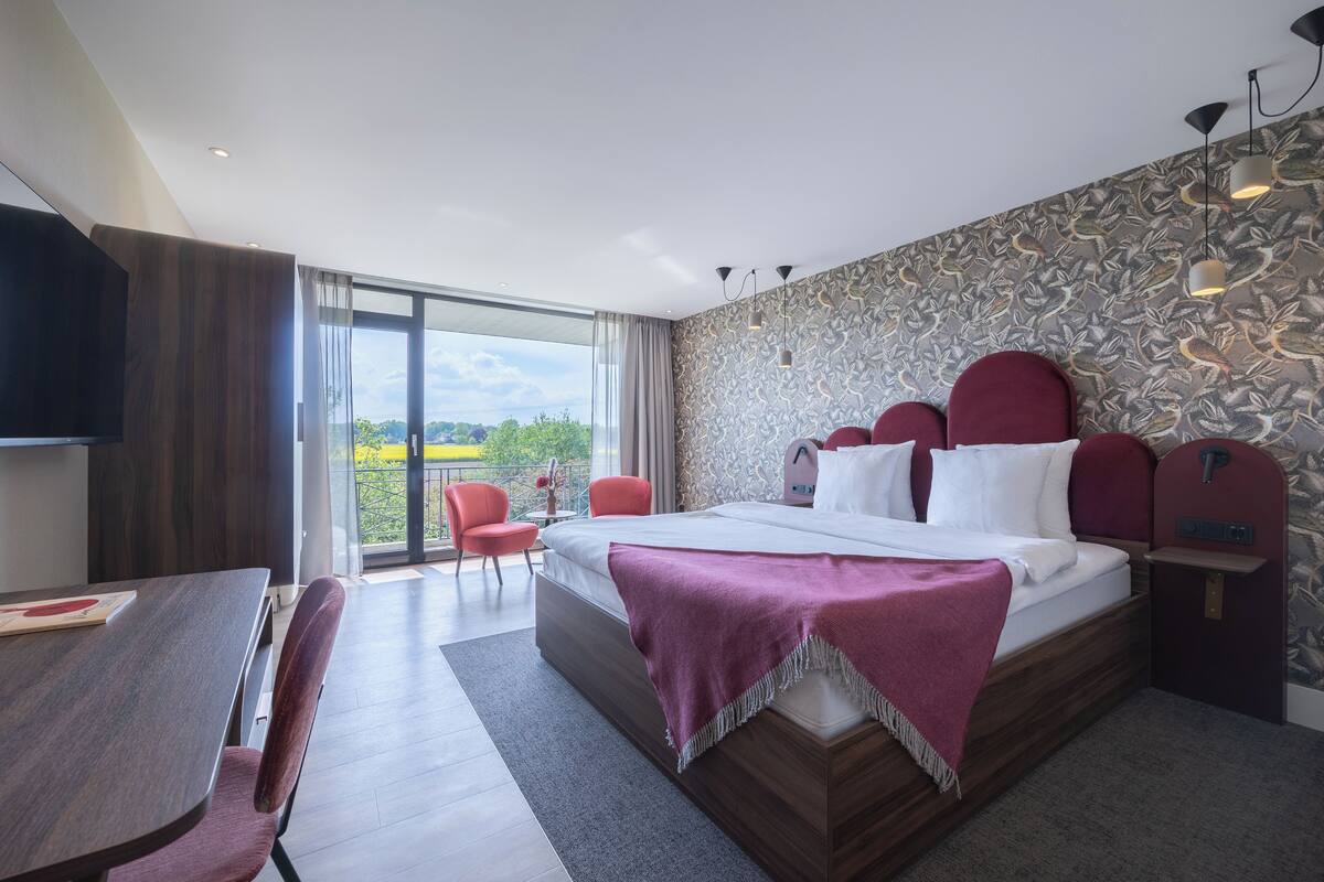 A modern hotel room with a large bed, a dining area, and a balcony with a view.
