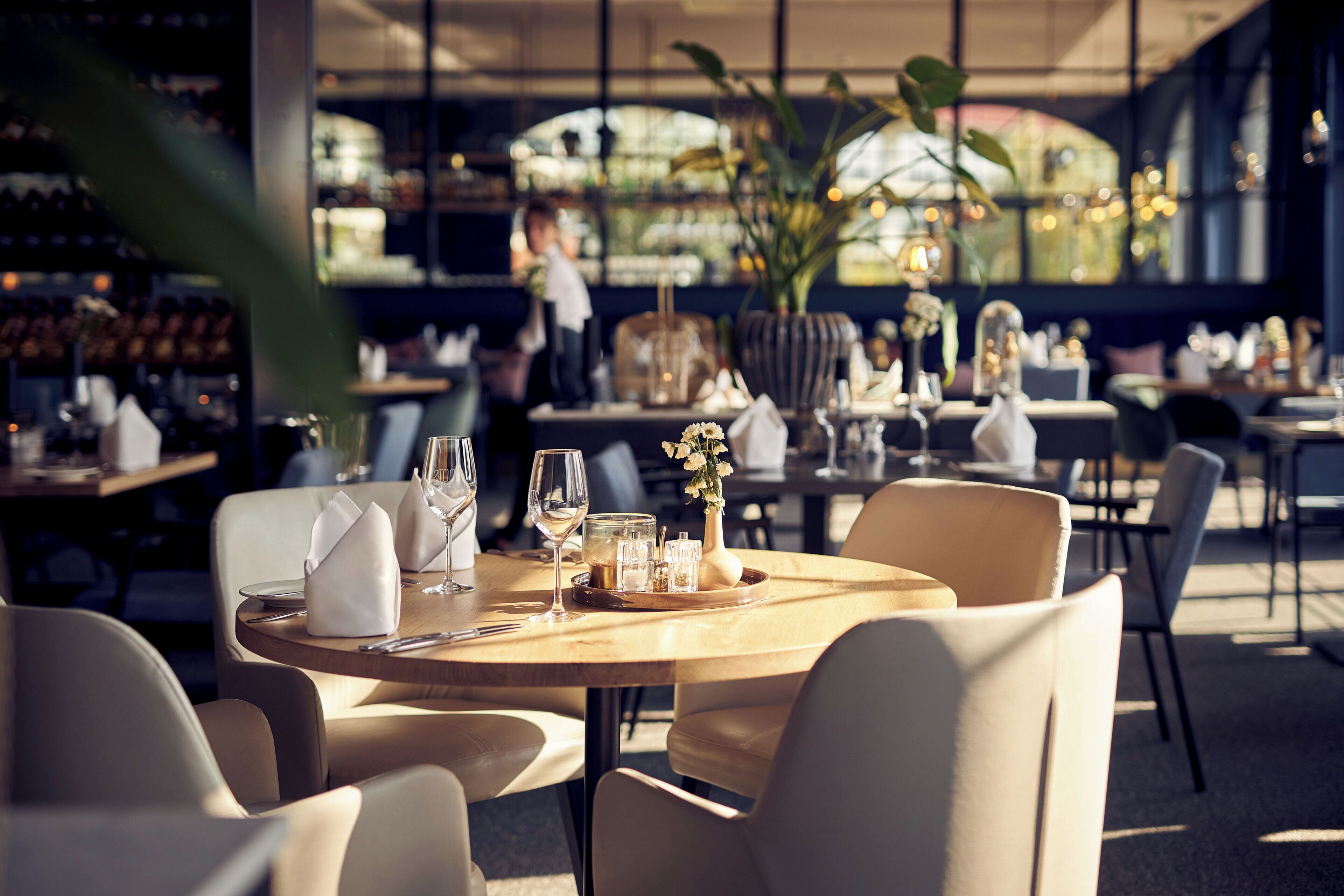 A restaurant with round tables, chairs, and a bar area in the background.