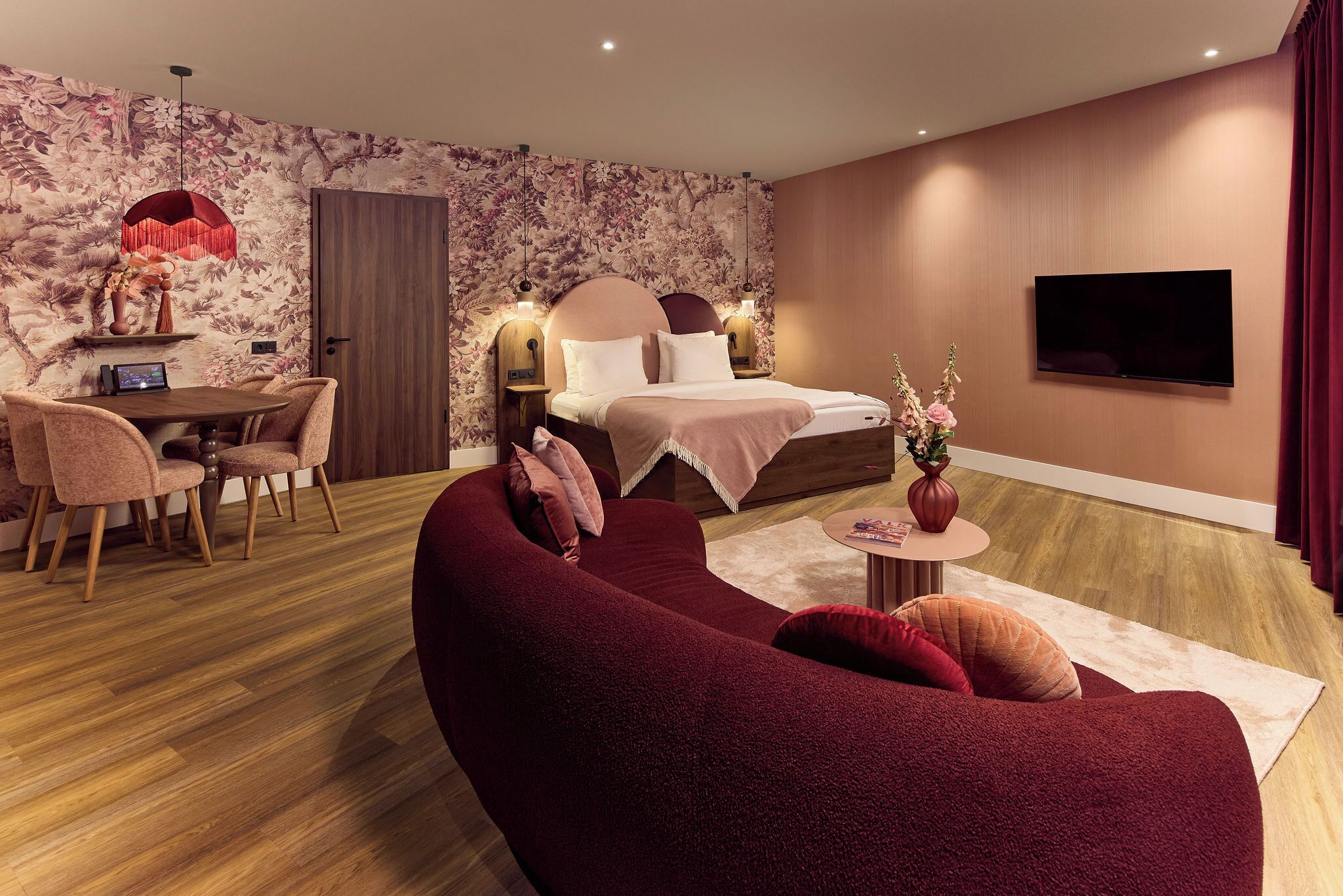 Een moderne slaapkamer met een bed, een televisie, een bank en een eethoek met stoelen en een tafel.