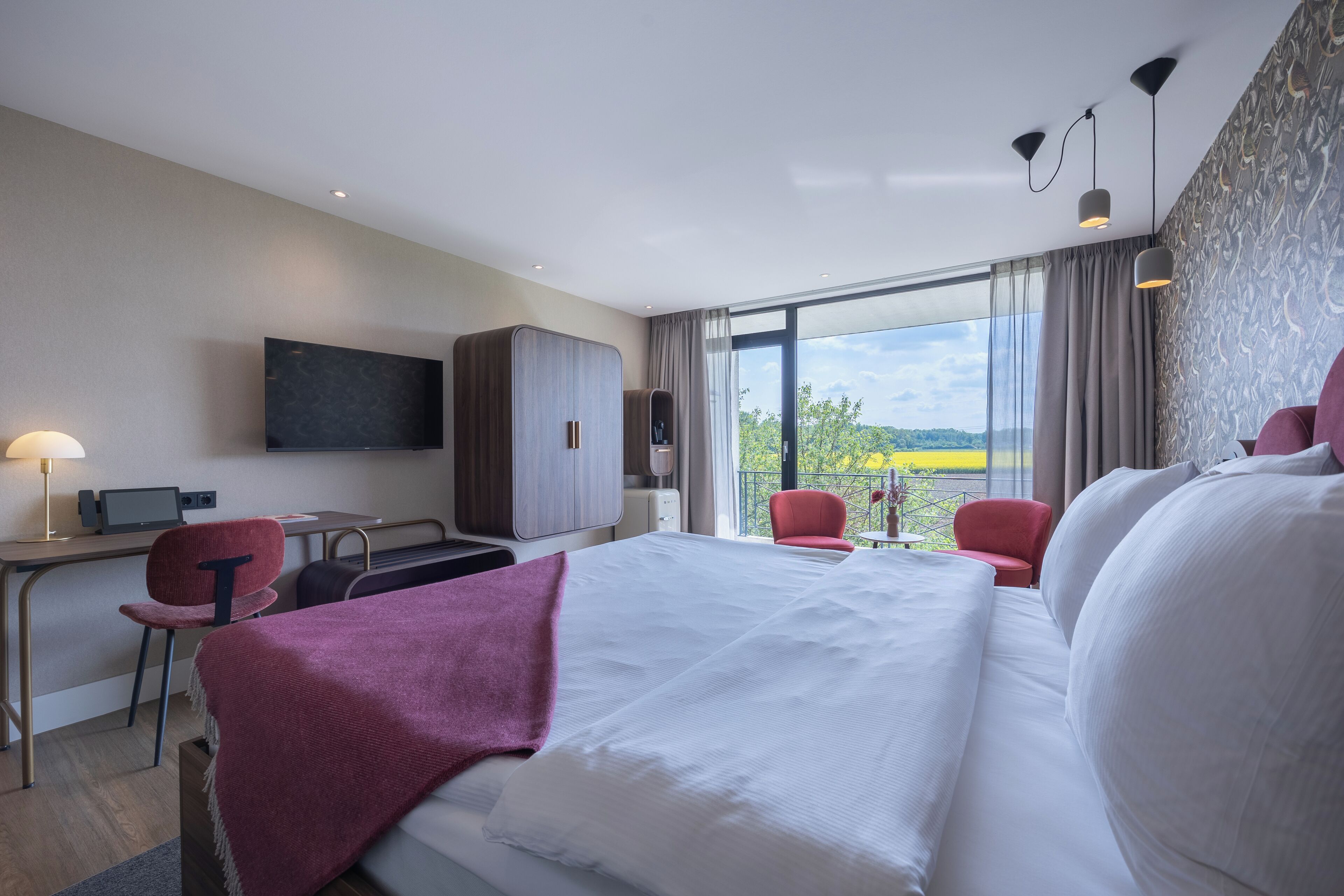 Een hotelkamer met een groot bed, een bureau, een stoel en een aan de muur bevestigde televisie.