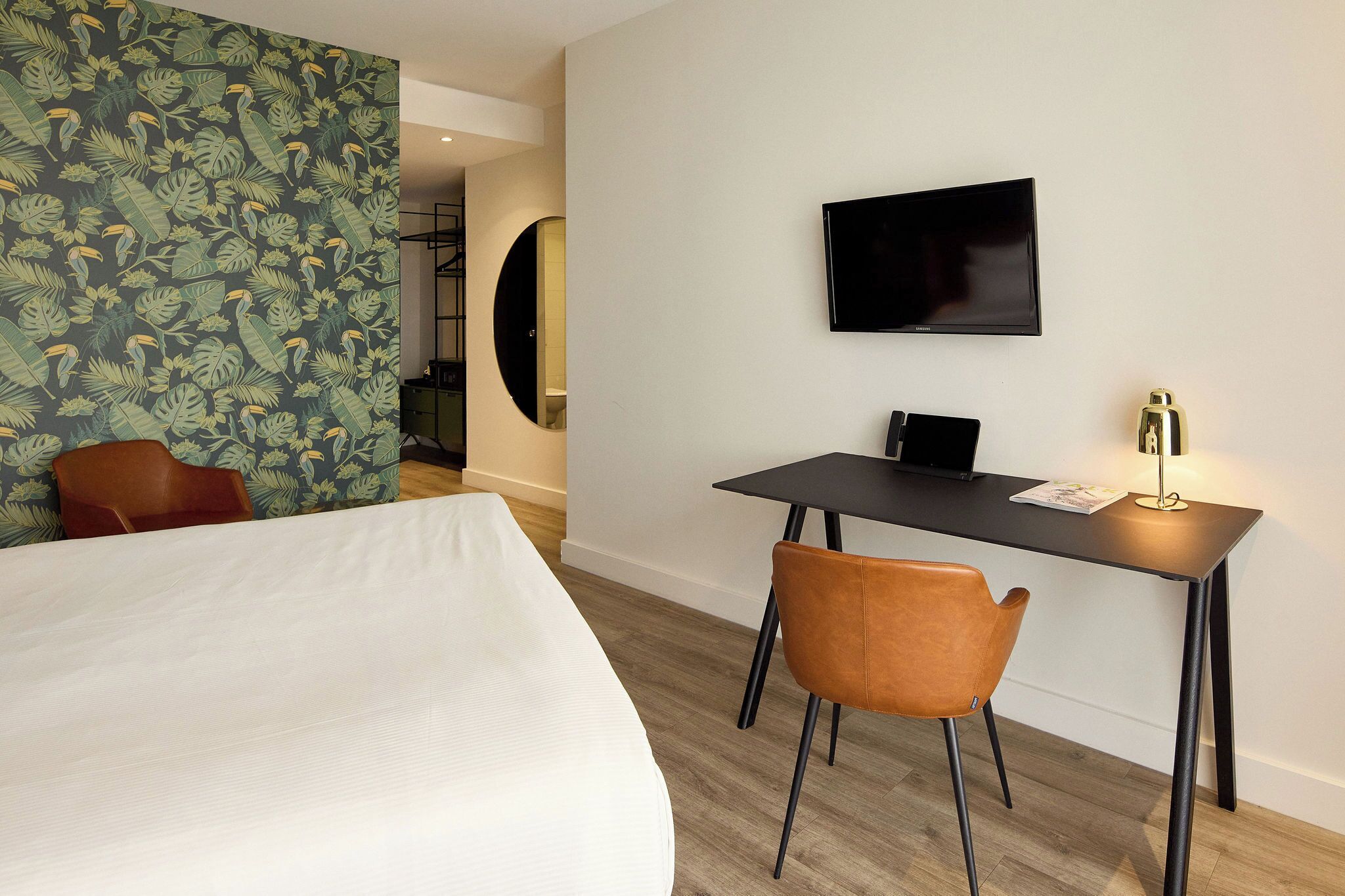 A hotel room with a bed, a desk with a chair, a TV, and a mirror.