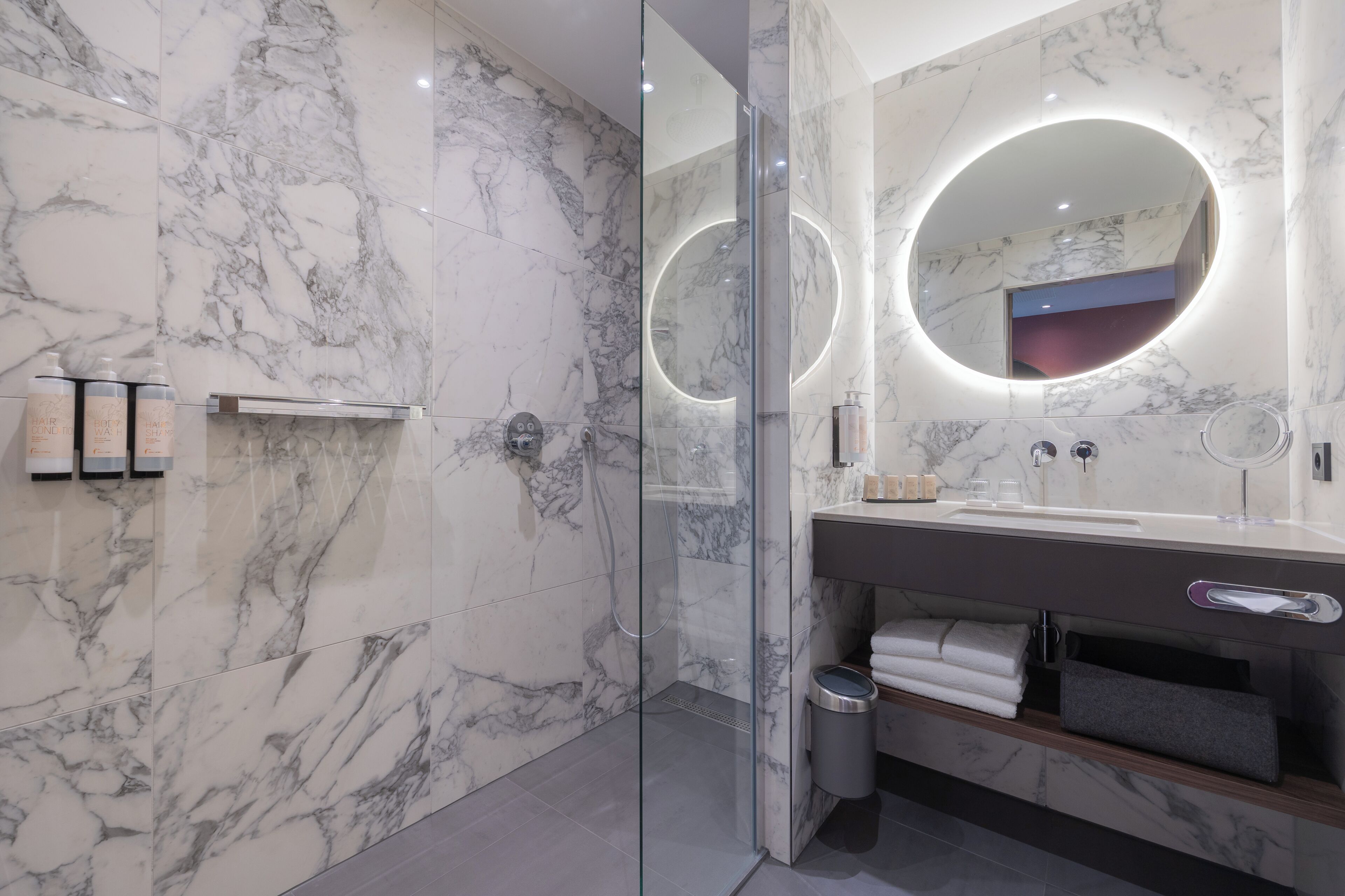 Une salle de bain moderne avec des murs en marbre, une douche en verre et un meuble-lavabo doté d’un miroir et d’un porte-serviettes.