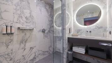 Une salle de bain moderne avec des murs en marbre, une douche en verre et un meuble-lavabo doté d’un miroir et d’un porte-serviettes.