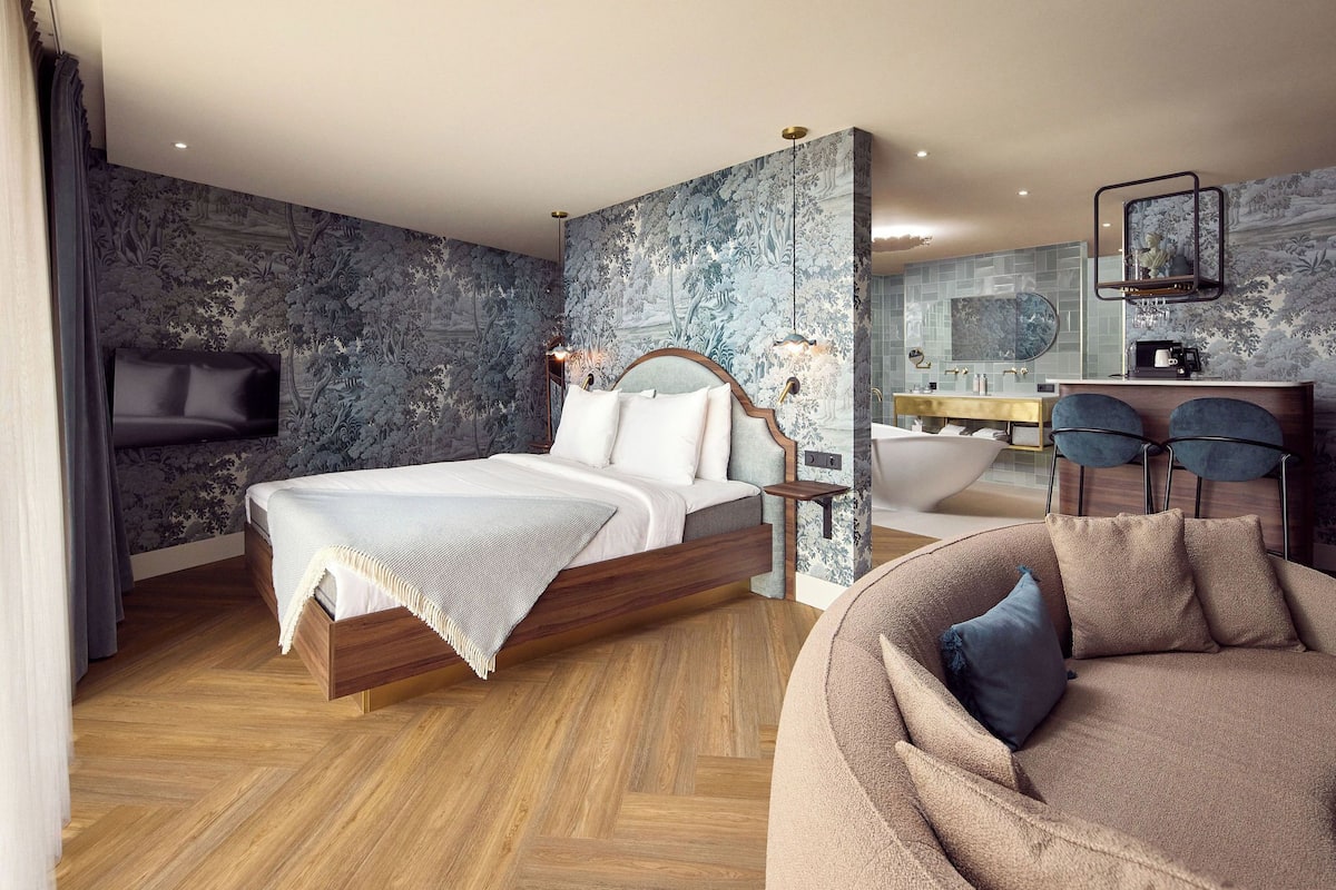 A modern bedroom with a bed, a sofa, a vanity, and a bathtub.