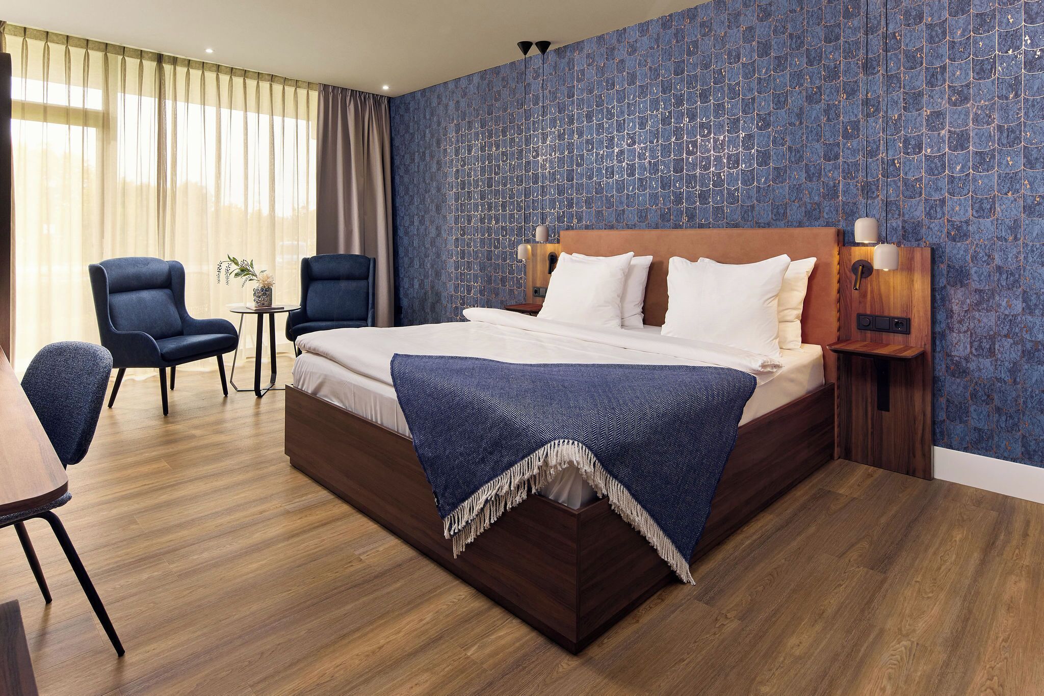 Ein Hotelzimmer mit einem großen Bett, zwei Sesseln, einem kleinen Tisch und einem Nachttisch mit Lampen.