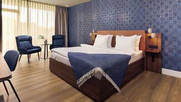 Ein Hotelzimmer mit einem großen Bett, zwei Sesseln, einem kleinen Tisch und einem Nachttisch mit Lampen.