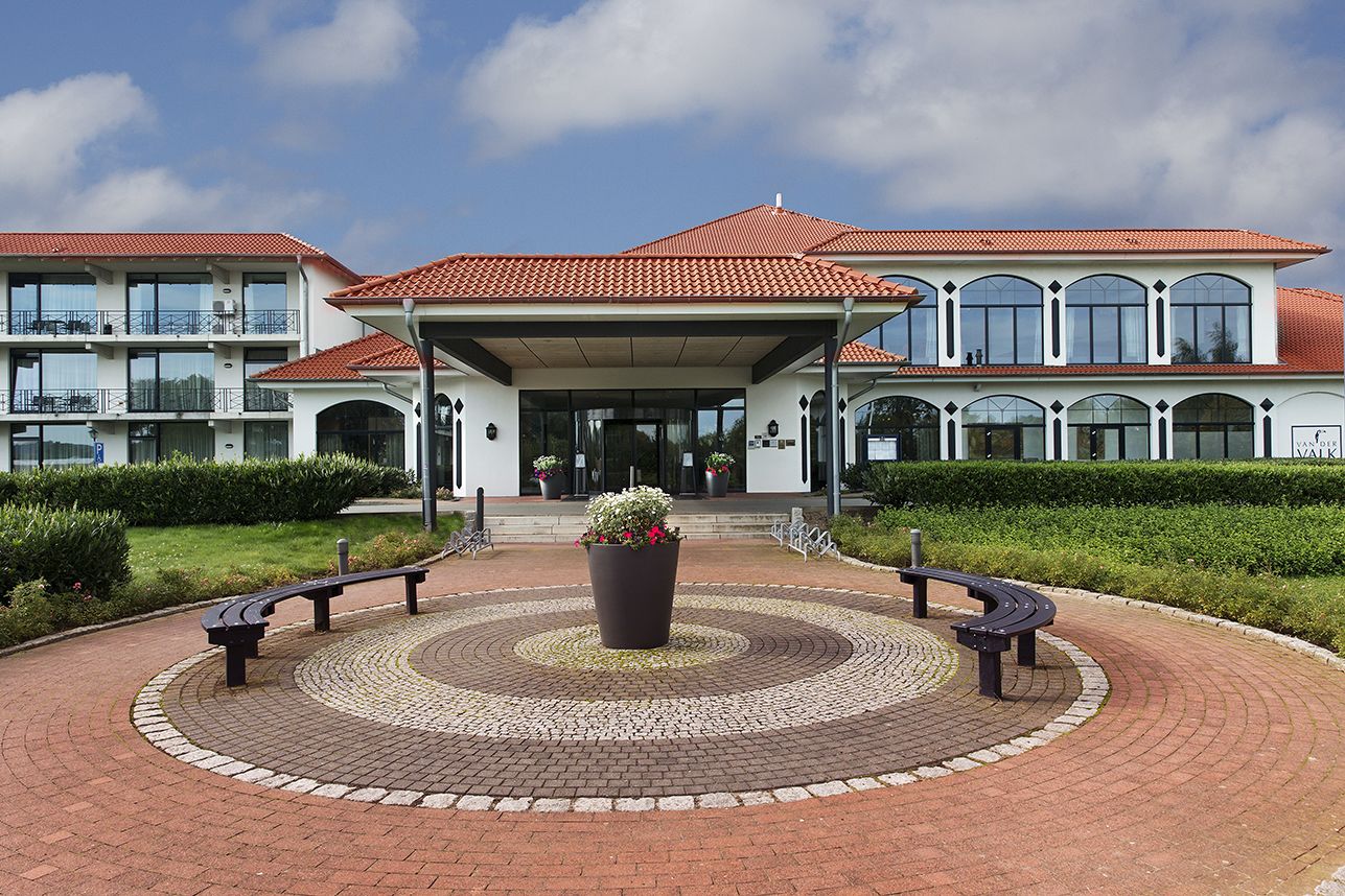 A hotel entrance with a circular brick pathway, benches, and a central planter.