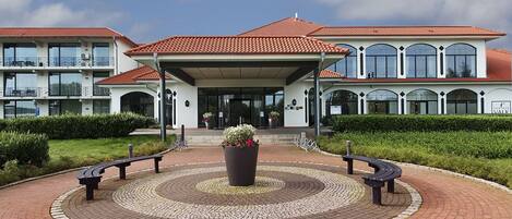 A hotel entrance with a circular brick pathway, benches, and a central planter.