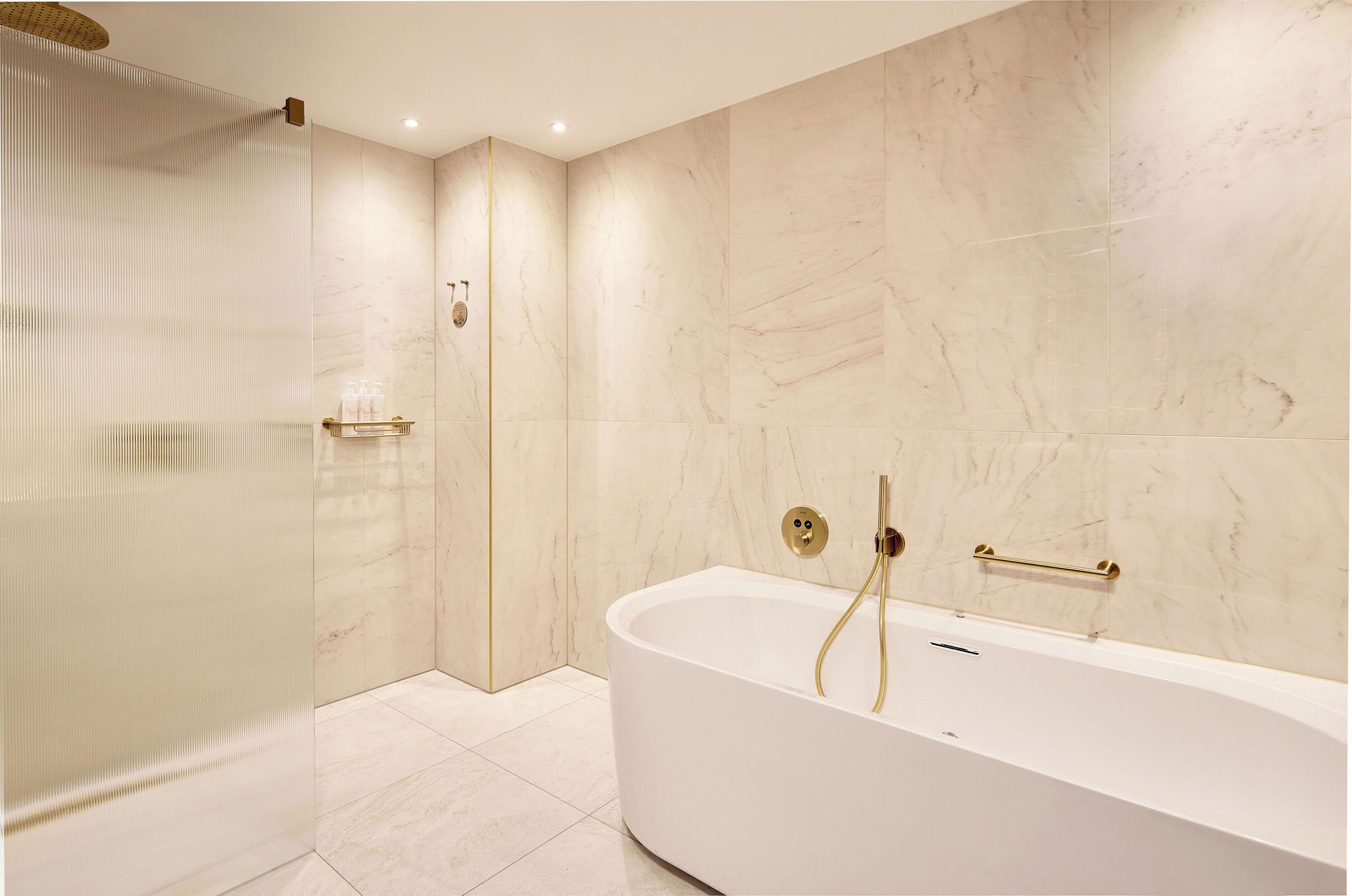 Un baño moderno con una bañera independiente, cabina de ducha con mampara de vidrio y paredes de mármol.