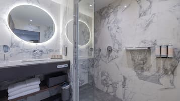 Uma casa de banho moderna com paredes de mármore, cabine de duche envidraçada e toucador com espelho e iluminação.