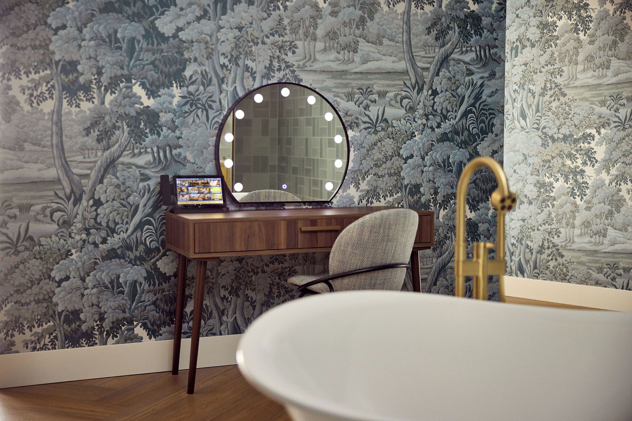 Ein Badezimmer mit Waschtisch, einem runden Spiegel mit Beleuchtung, einem Sessel und einer Badewanne.