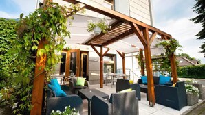 An outdoor patio area with wicker furniture, a wooden pergola, and hanging plants. - Hotel Perla (Kraków)