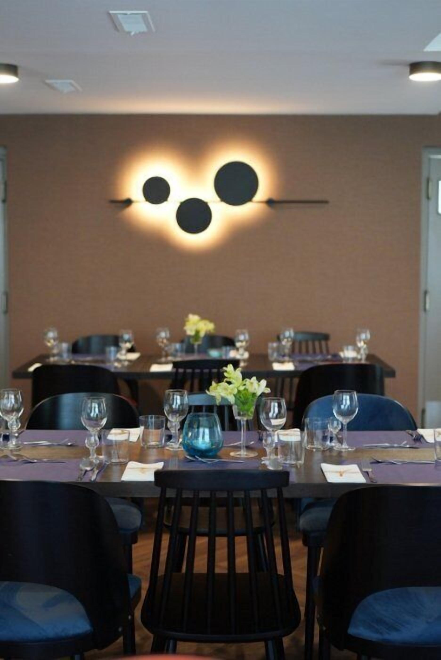 A dining area with tables set for four, each with chairs, glasses, and a vase of flowers.