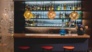 A bar area with shelves of liquor bottles, two hanging lamps, and a bar counter with stools. - Hotel Perla (Kraków)