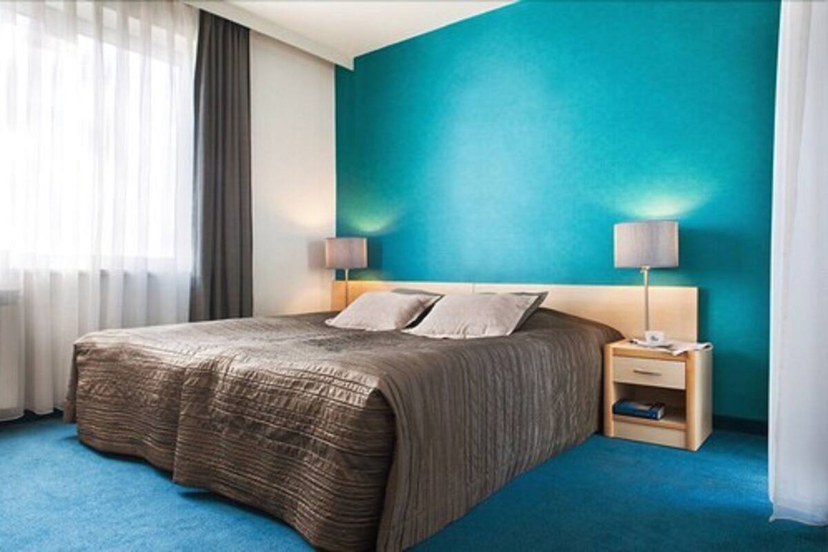 Habitación de hotel con una cama grande, dos mesitas de noche y una pared de acento color aguamarina.