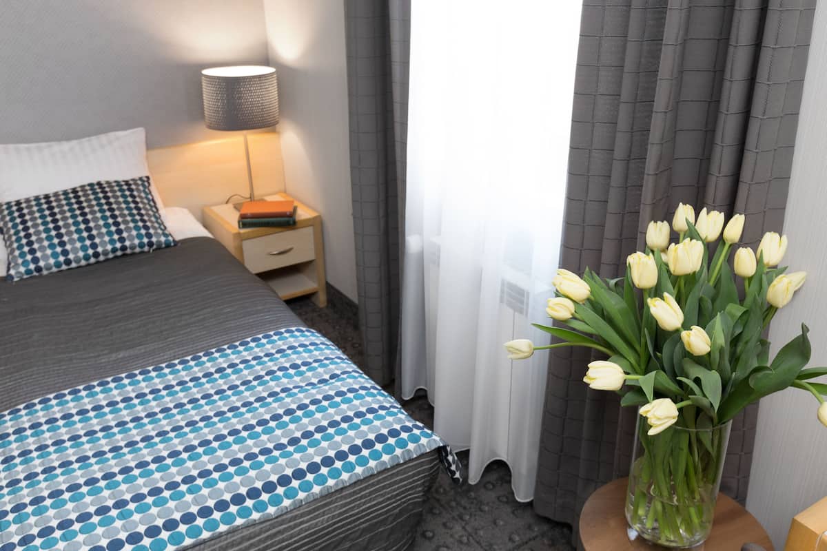 Una habitación de hotel con una cama, una mesita de noche, una lámpara y un jarrón con tulipanes.
