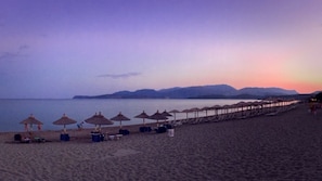Na praia, espreguiçadeiras, guarda-sóis, prática de vôlei de praia