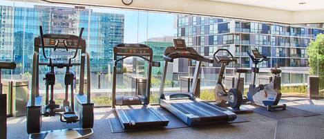 Un gimnasio con cintas de correr, elípticas y equipo de pesas, que cuenta con amplios ventanales con vistas a la ciudad.