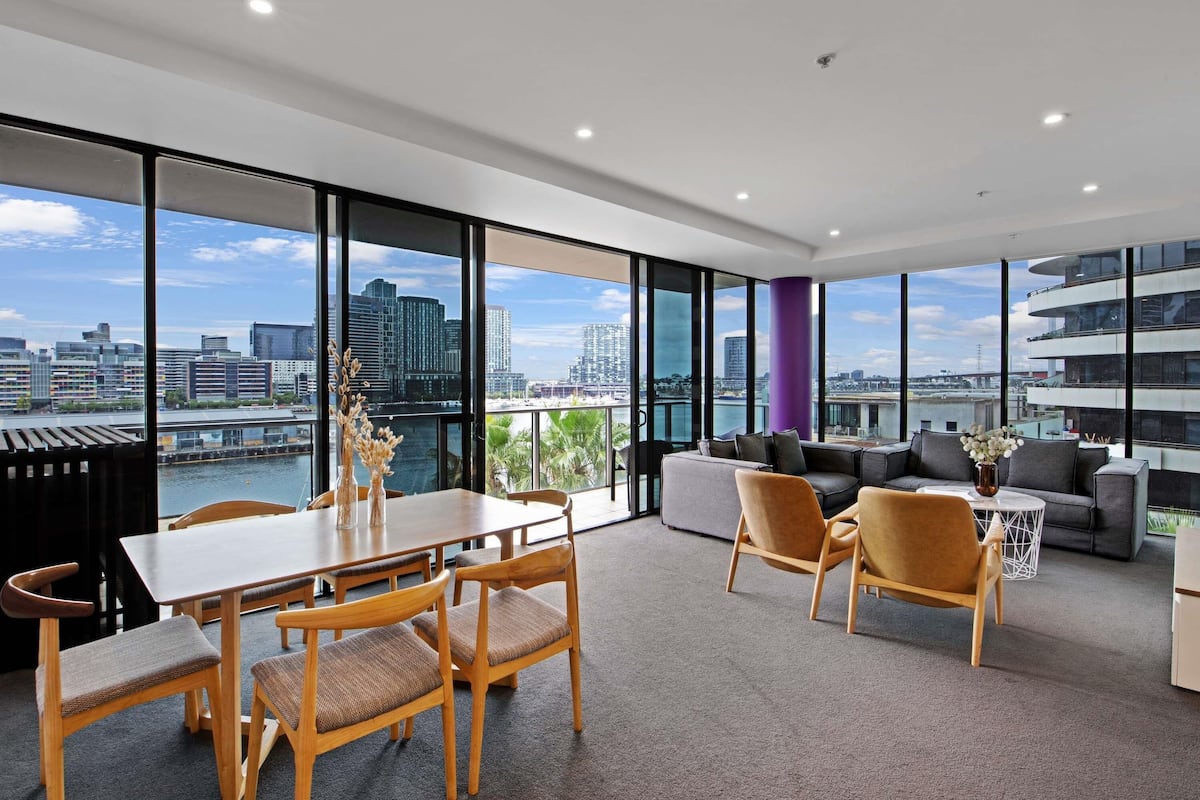 Ein modernes Hotelzimmer mit Essbereich, einer Sofagarnitur und großen Fenstern mit Blick auf die Stadt.