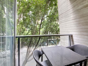 A balcony with a wicker table and chairs, a glass door, and a view of trees and buildings.