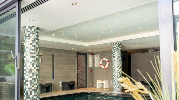 Un espace piscine intérieur moderne, avec des piliers à motifs à carreaux, une bouée de sauvetage et une enceinte en verre.
