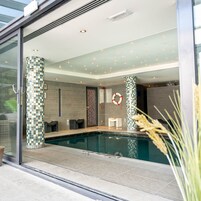 Un área de piscina interior moderna con pilares a cuadros, un flotador salvavidas y un cerramiento de vidrio.
