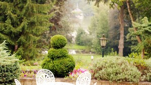 Un jardin avec des haies soigneusement taillées, un lampadaire et une vue lointaine d’un bâtiment.