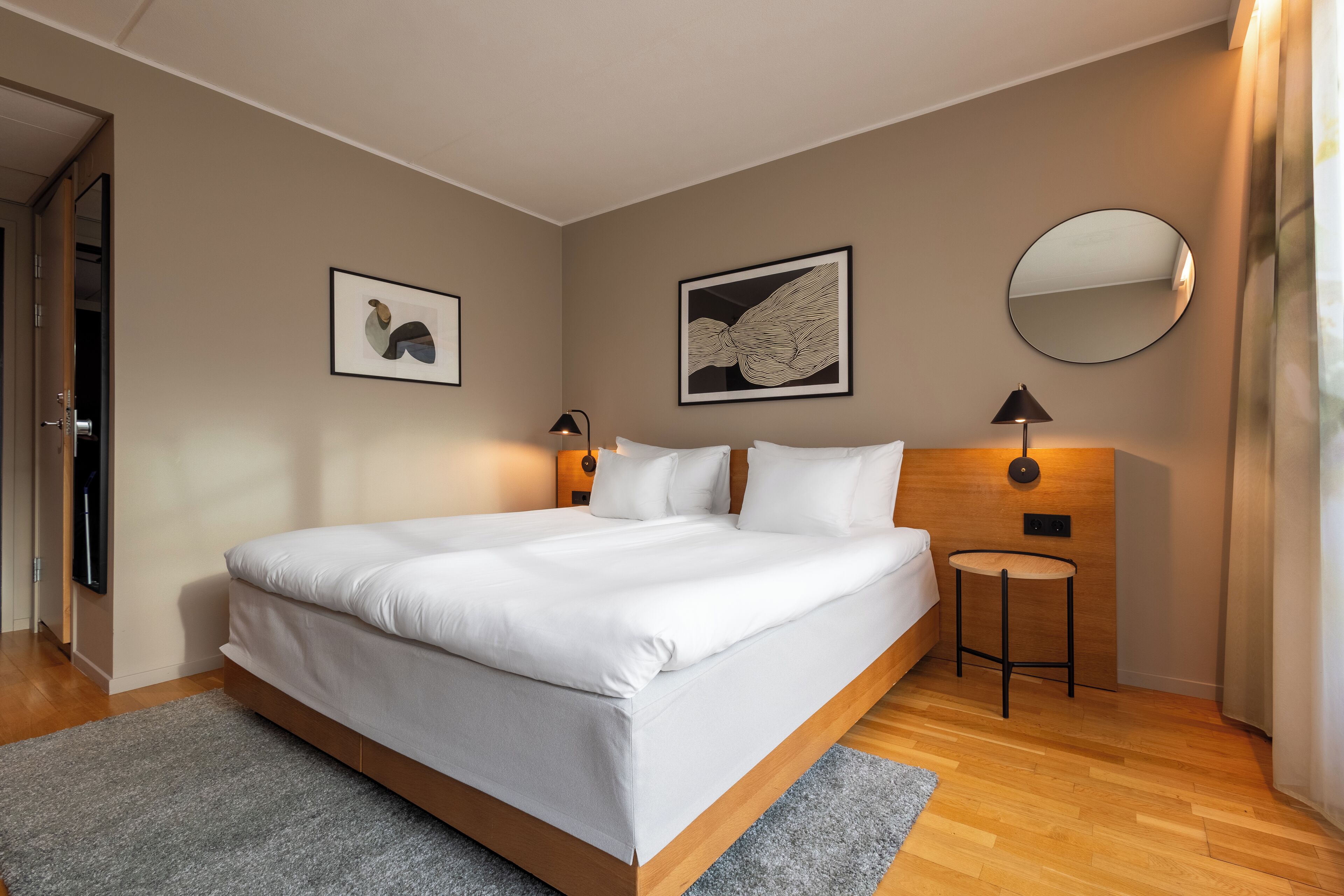 A modern bedroom with a large bed, two wall-mounted lamps, and two framed artworks.