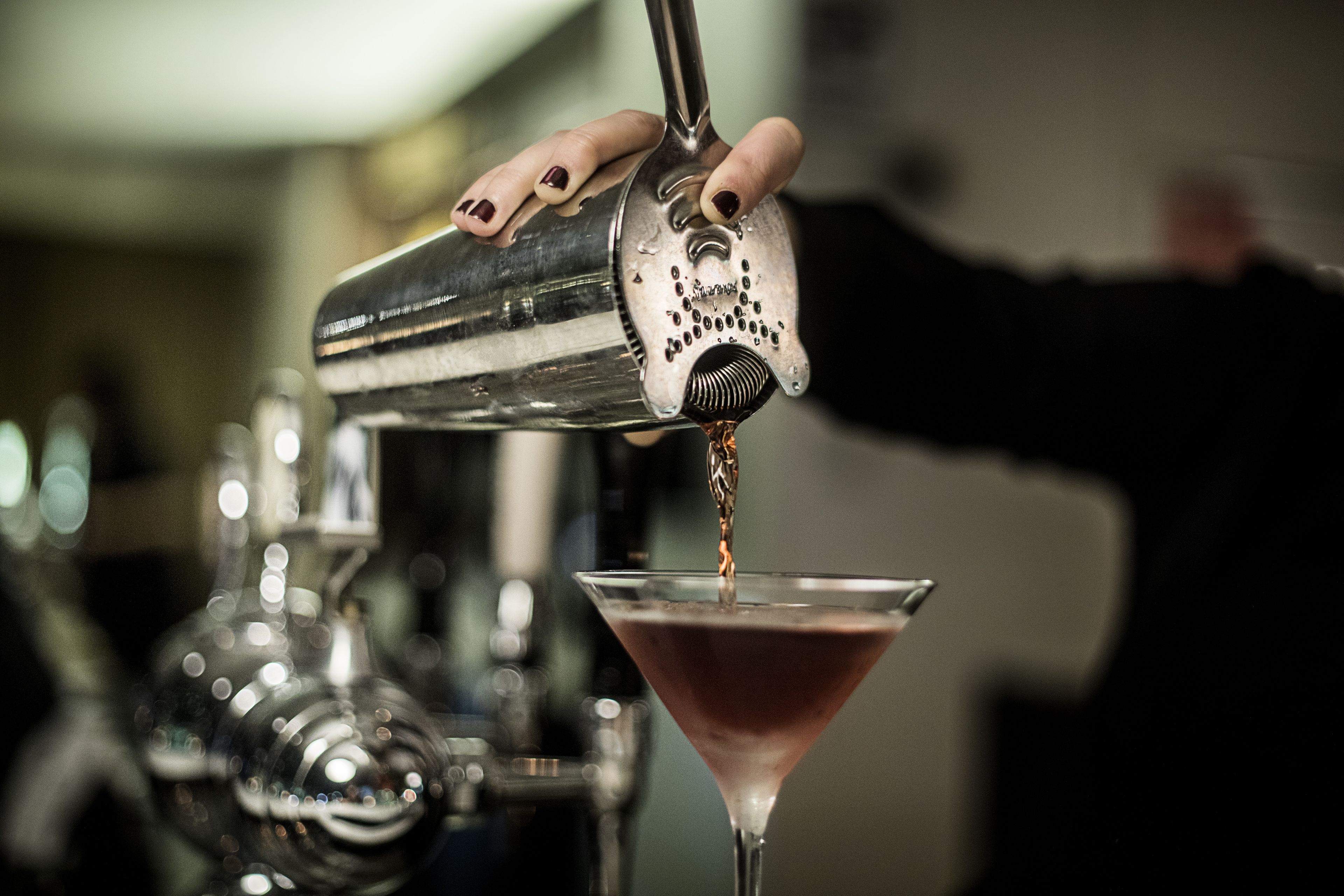 En bartender som häller upp en drink i ett martiniglas.
