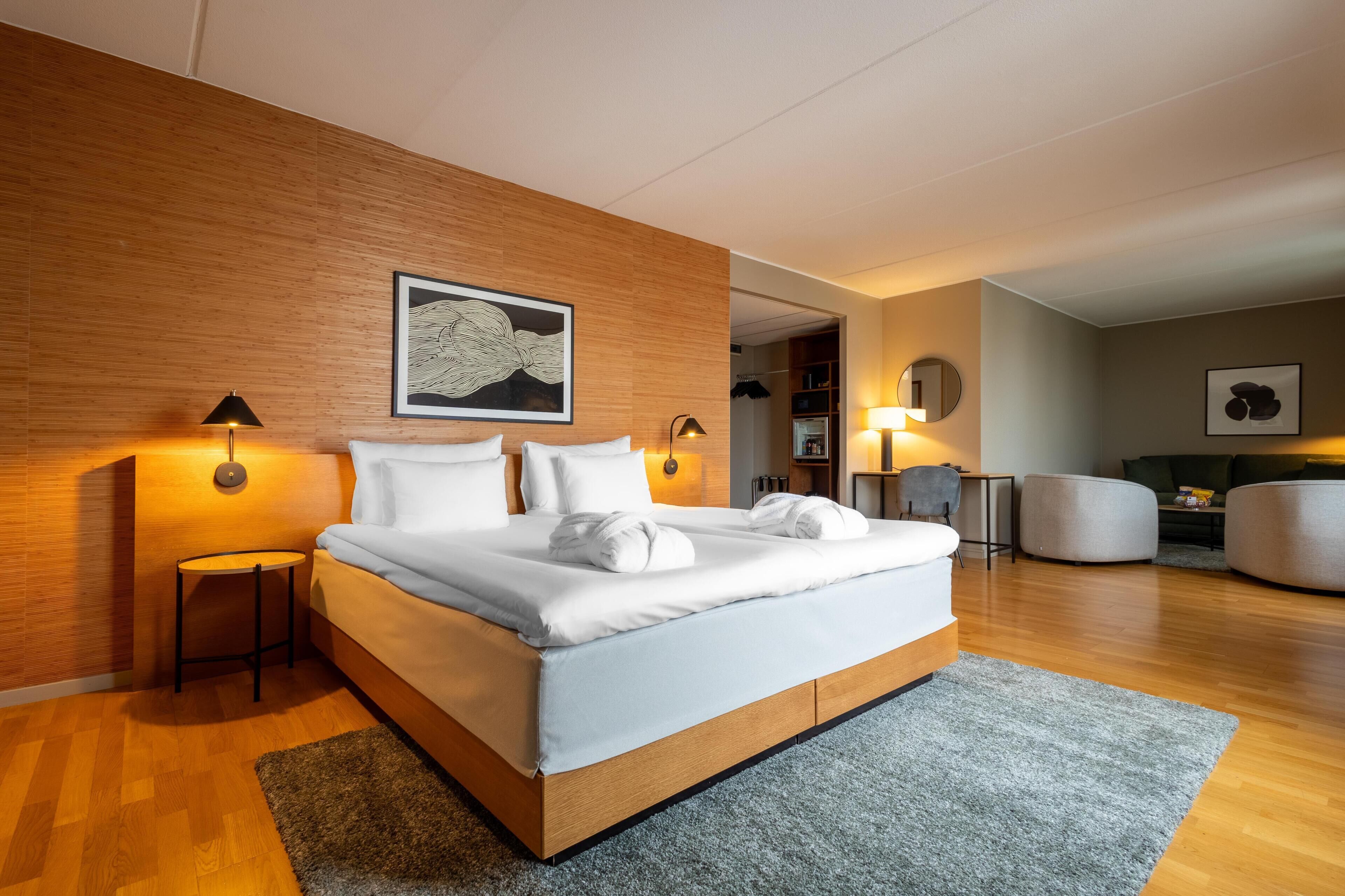A modern hotel room with a large bed, two bedside lamps, a wooden accent wall, and a framed artwork.