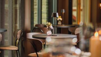 Un interior de restaurante con mesas redondas, sillas, un florero y una vela.