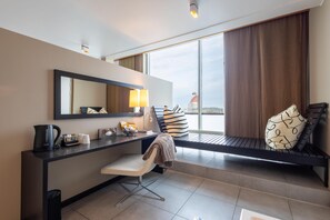 Une chambre d’hôtel moderne, dotée d’un bureau, d’une chaise et d’une grande fenêtre donnant sur la ville.