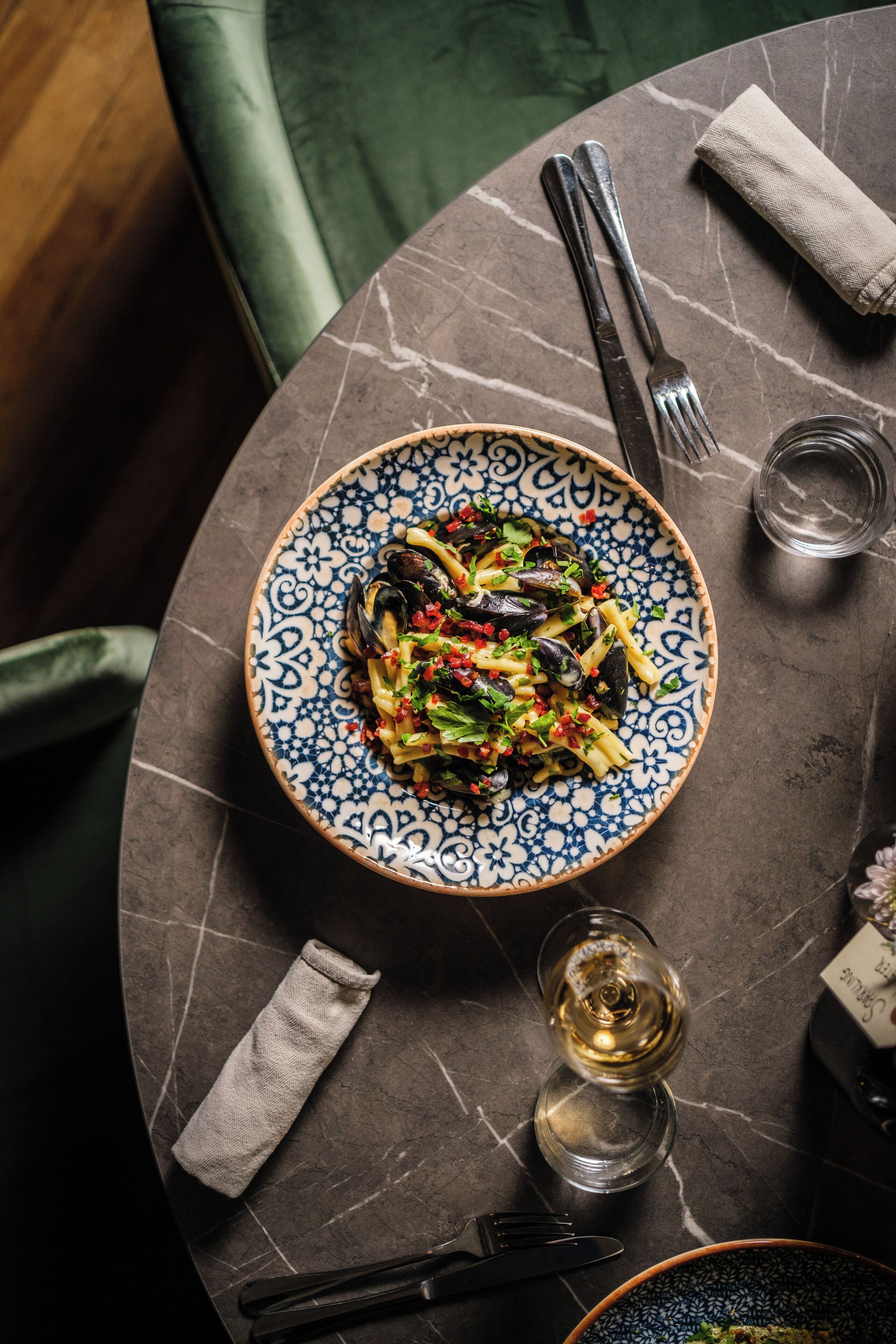 Una mesa de comedor con un plato de pasta, una copa de vino y cubiertos.