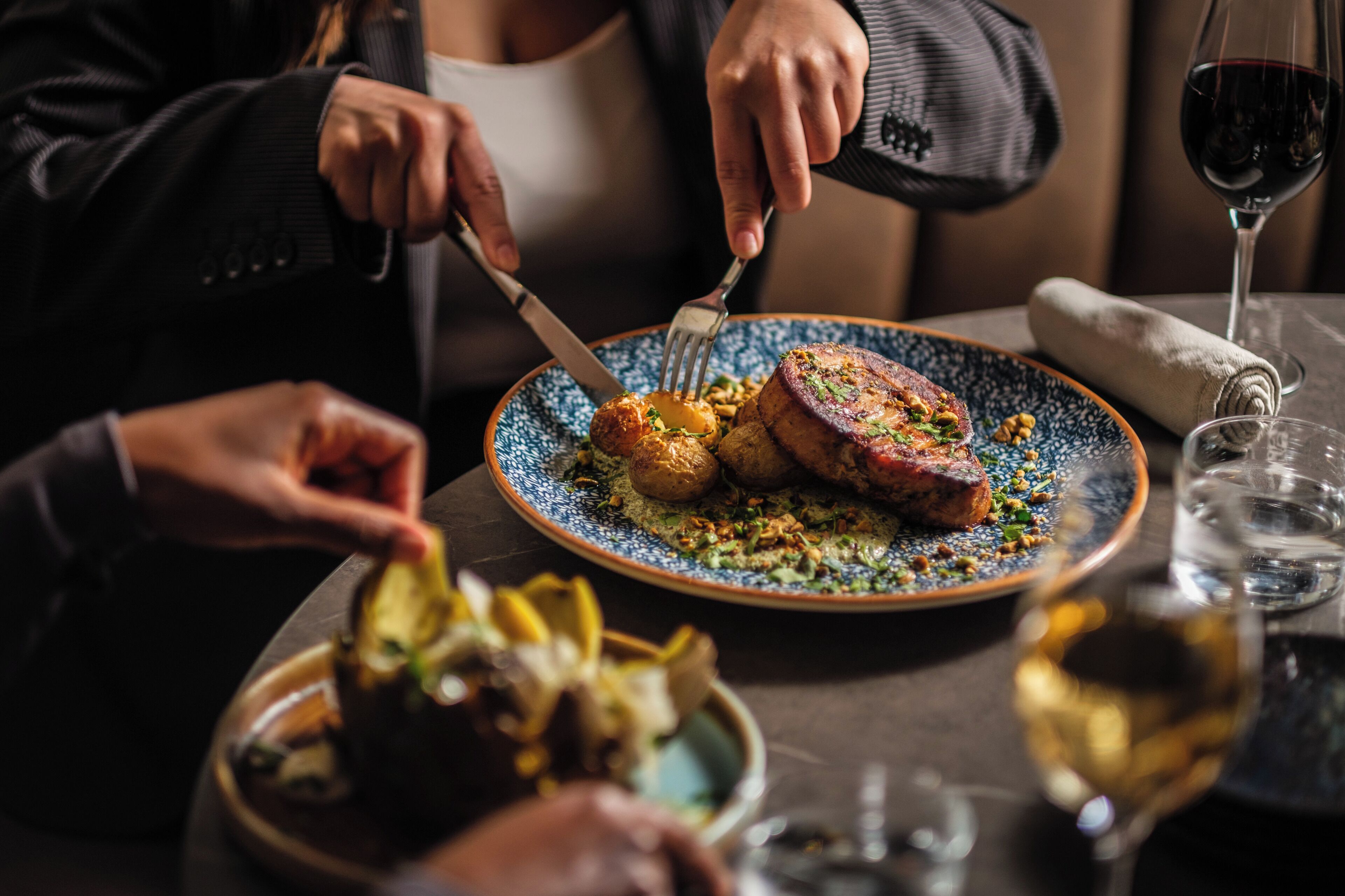 A dining table with a plate of food, a glass of red wine, and a napkin.