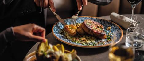Una mesa de comedor con un plato de comida, una copa de vino tinto y una servilleta.